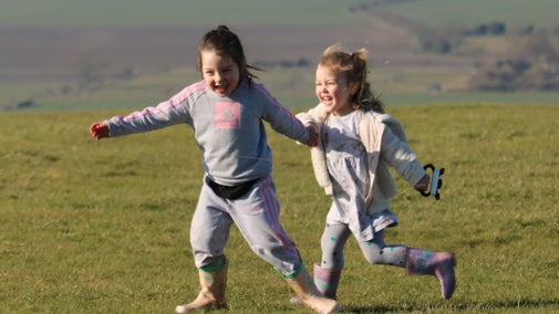 two young girls running on a field in wellies.